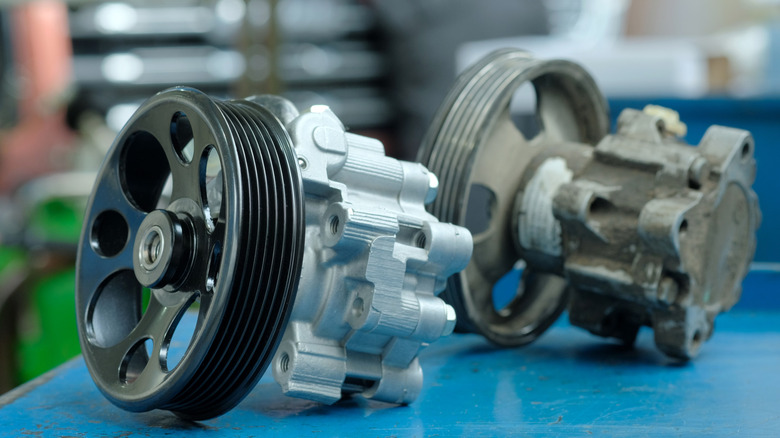 New and old power steering pumps on table, new one in-focus with old one positioned behind and to the right