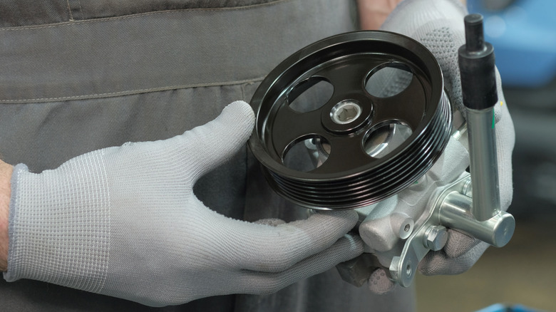 Mechanic with gloved hands holding power steering pump