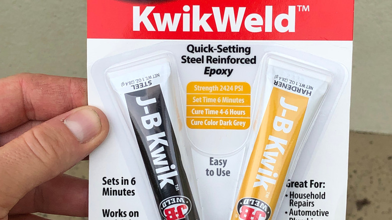 A hand holding a package of J-B Weld KwikWeld epoxy tubes