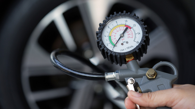 A person checking the air pressure reading while inflating a tire