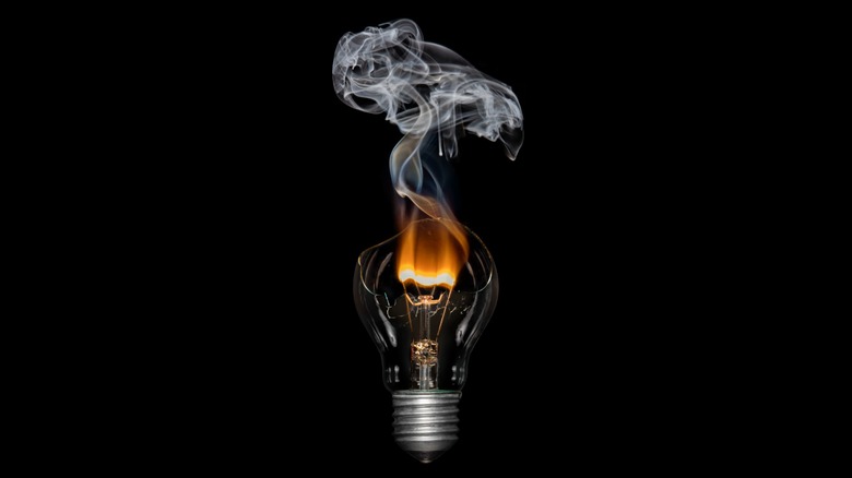 Blown filament bulb emitting smoke against a black background