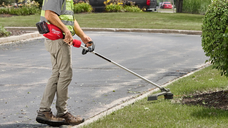 Professional landscaper using a Milwaukee M18 Fuel 16 inch string trimmer