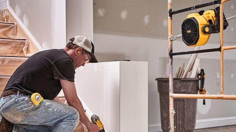 A man using a tool on a staircase while a DeWalt Battery-Powered Fan is hanged for cooling