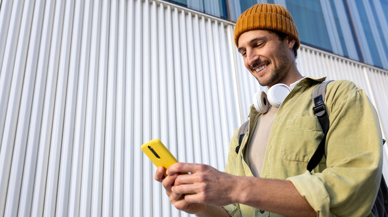 man walking outside, smiling and holding a smartphone