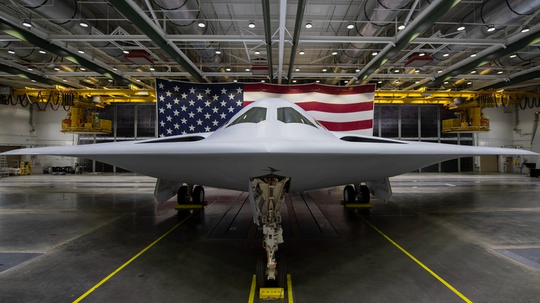 A B-21 Raider in a hangar with an American flag draped behind