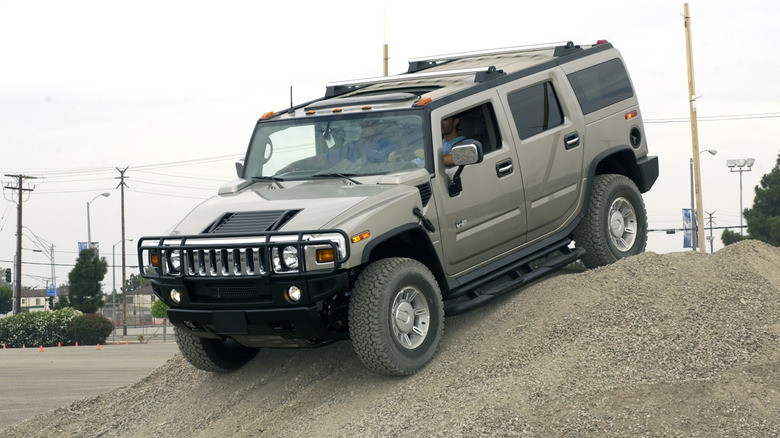 A Hummer H2 on an improvised gravel hill, front 3/4 view, greenish gray exterior