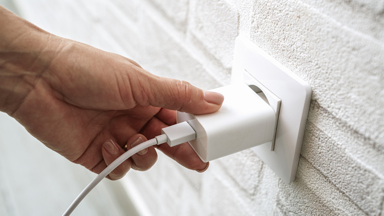 Hand holding a USB charger plugged into a wall outlet