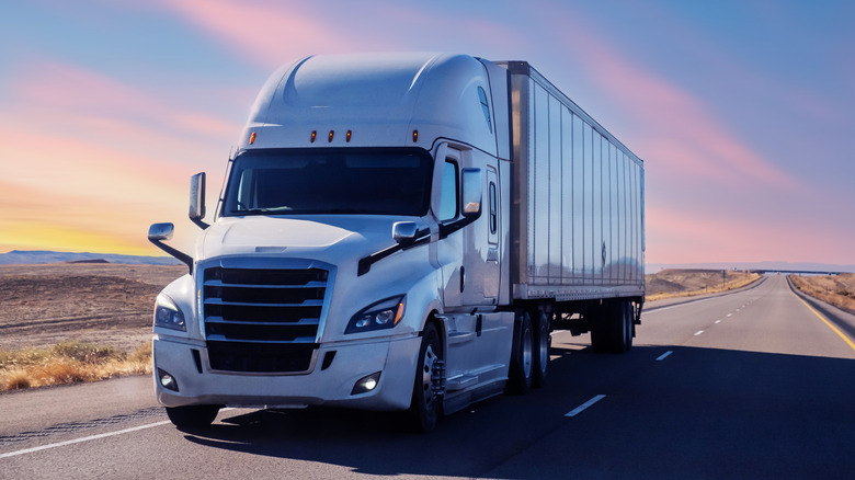White semi truck driving down a desert highway at sunset