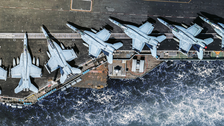 A line of F/A-18 Hornets on the edge of an aircraft carrier