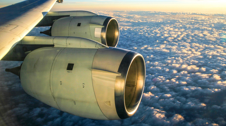 Two jet engines under an airplane wing, high above the clouds
