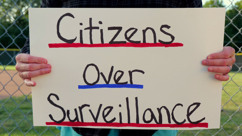 A protestor holds a sign that reads "Citizens over surveillance"