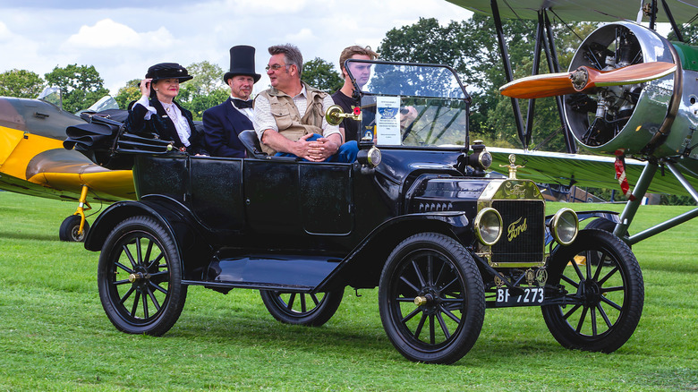 Group of people riding a Model T on a grassy field