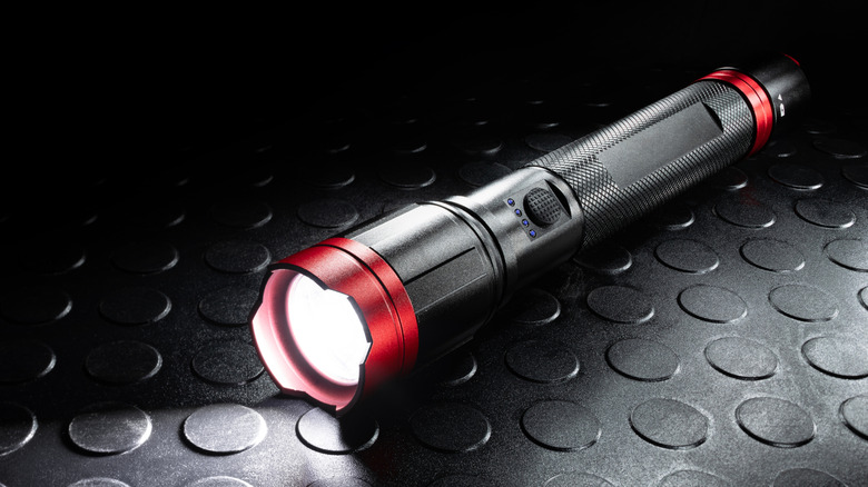 A black and red colored flashlight emitting a white beam in the dark