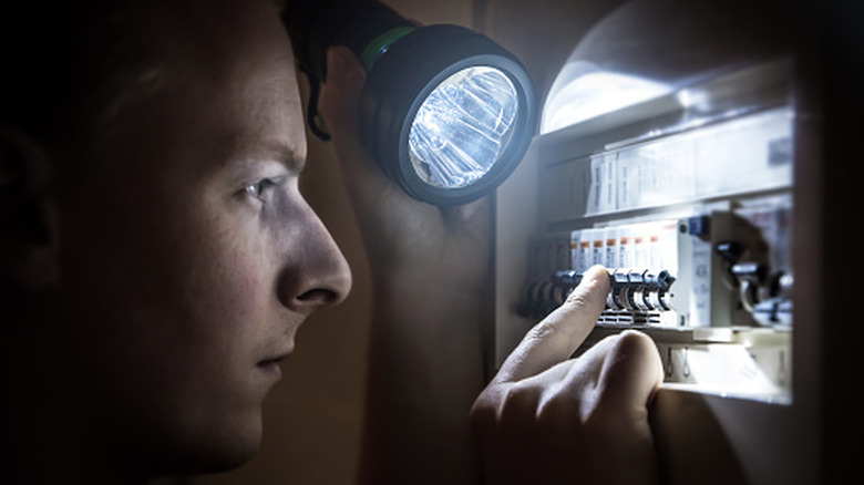 A man using a flashlight while looking at a circuit breaker