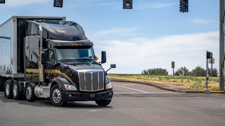 Black semi-truck going through intersection under traffic lights
