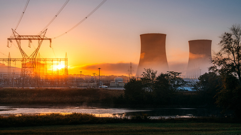 A nuclear power plant at sunset with cooling towers and pylons prominent.