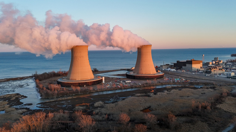 A nuclear power plant by the sea with two cooling towers emitting steam.