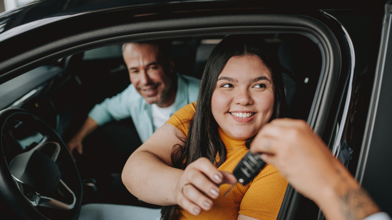 Young woman being handed car keys through open driver's window