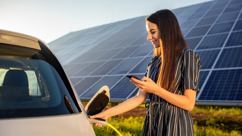 person charging EV next to solar panels