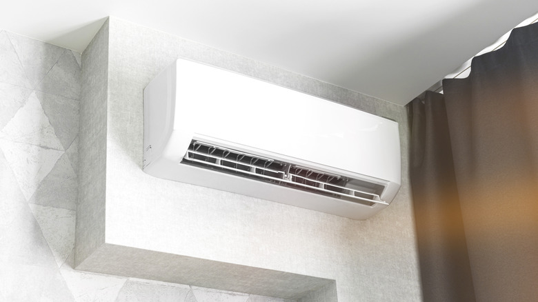A white mini split vent against a white wall, next to a dark drawn curtain