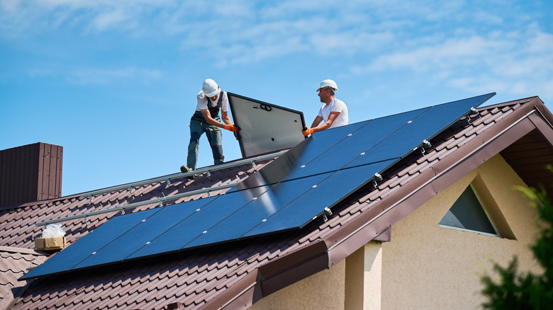 Two men installers in helmets carrying photovoltaic solar module outdoors.