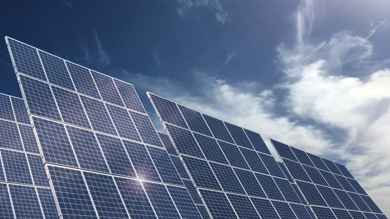 An array of solar panels pointed at the sun, clouds in the background