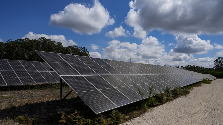A shot of twin banks of solar panels shown on a sunny day with a handful of clouds in the sky
