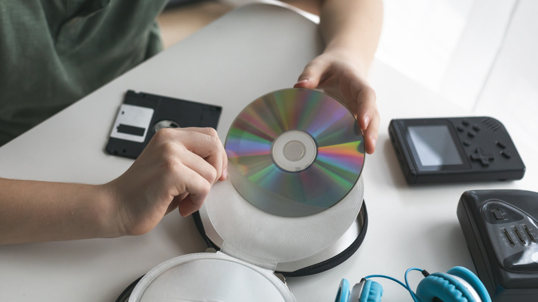 A person holding a CD data side up surrounded by other retro gadgets