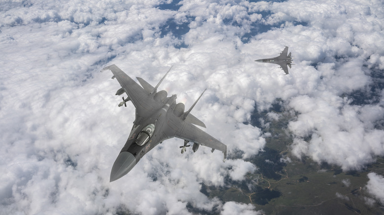 A pair of Su-35 aircraft flying over thick cloud formations.