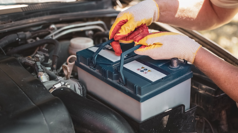 A mechanic wearing gloves installing a car battery