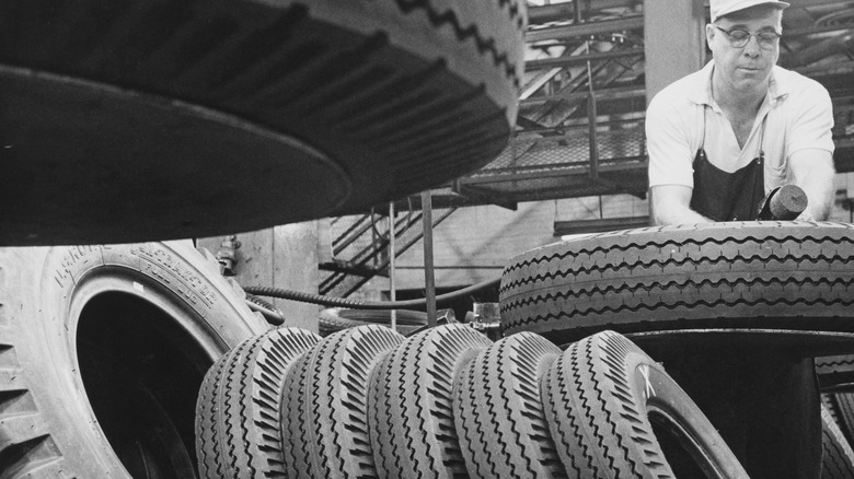 Black and white image of an old tire factory with an employee working on a tire.