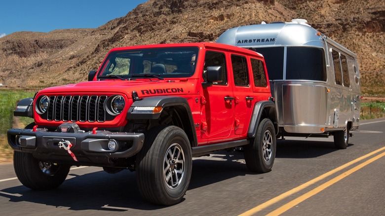 2024 Jeep Wrangler Rubicon in red towing a small Airstream trailer