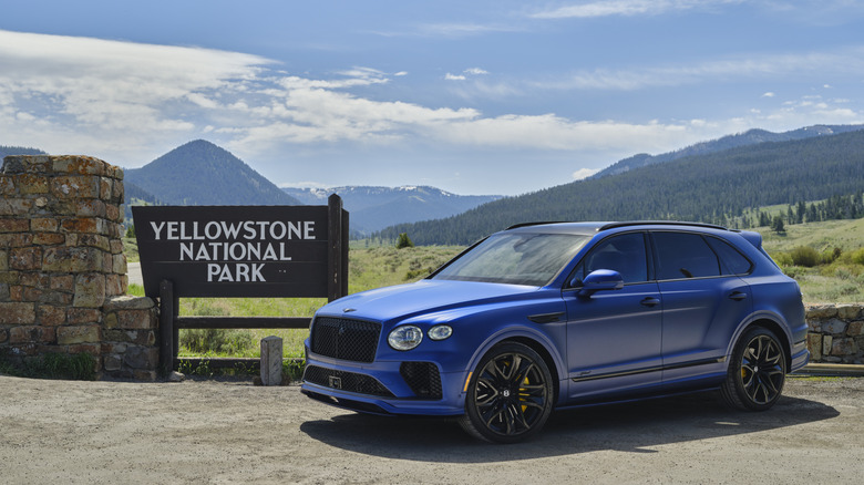 Sequin Blue Satin Bentley Bentayga parked next to the sign for Yellowstone National Park