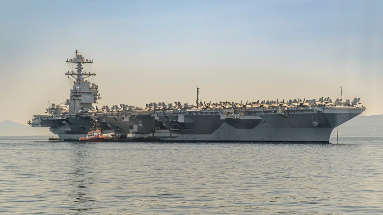 The USS Gerald R Ford aircraft carrier anchored just outside a port.
