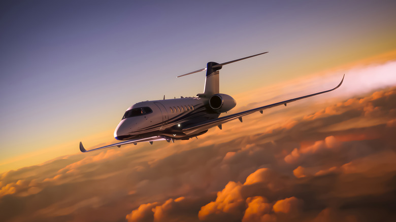 A private jet flying over clouds at sunset