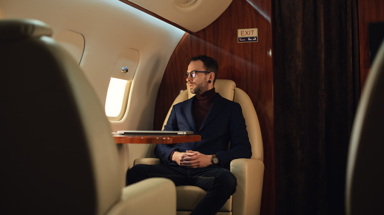 A man in a blue jacket looking through a private jet window