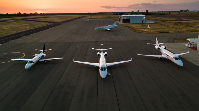 Four private jets parked on the runway at sunset
