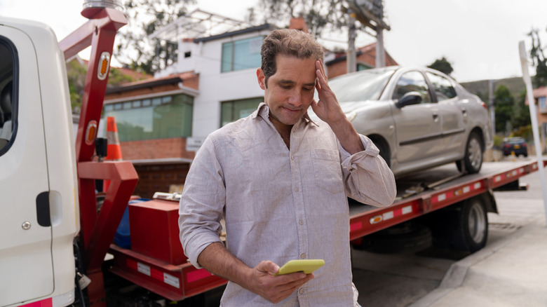 Man having problem with his car and calling roadside assistance to take his vehicle to the auto repair shop.
