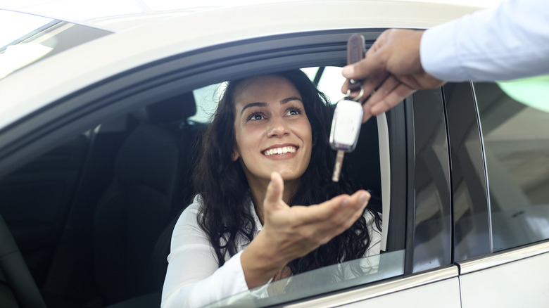 A smiling customer inside of their new car, dealership employee handing over the keys