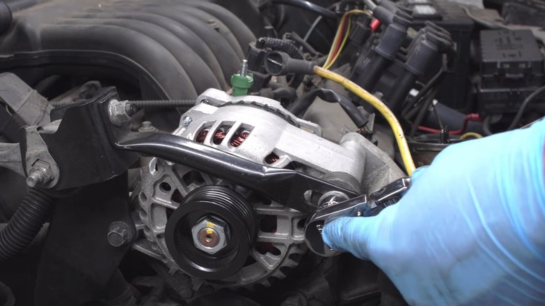 A person loosening the mounting bolts on an alternator