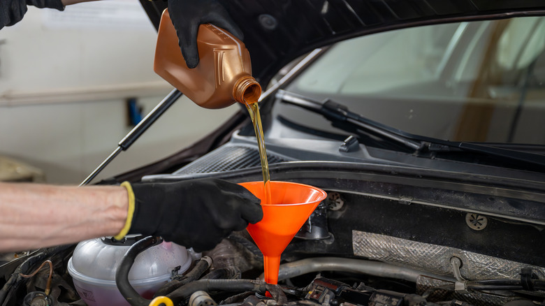 Gloved mechanic pouring motor oil into a car engine using an orange funnel