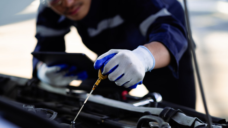 A mechanic in blue overalls checking the oil in a car using the dipstick