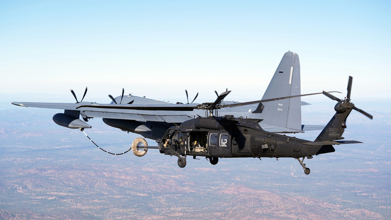 Rear view of USAF MC-130J Commando II refueling a Blackhawk helicopter in the air.