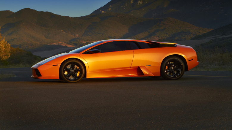 The side profile of an orange Lamborghini Murcielago parked outdoors during a sunset