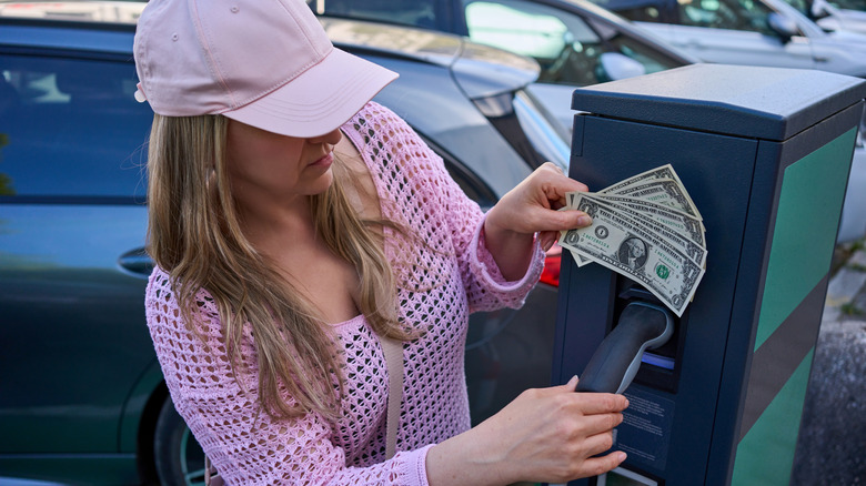A woman displaying a handful of dollar bills while holding an EV charging outlet.