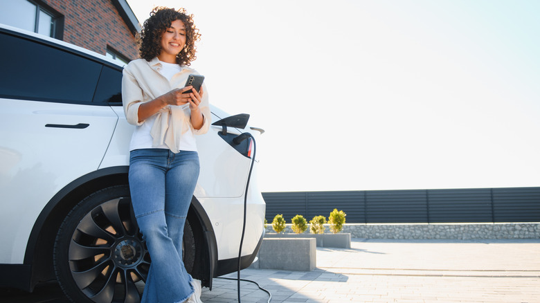A woman using her smartphone while charging her car at home