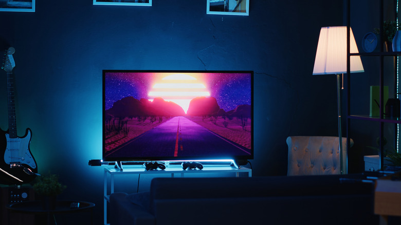 TV running in a room with neon lighting between a lamp and guitar placed close by