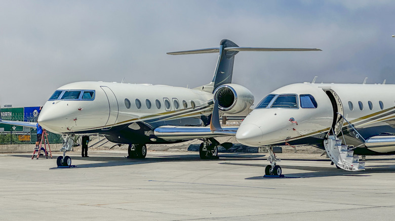 2 white and blue private jets parked on a runway