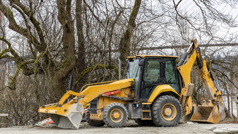 A larger backhoe loader parked in front of a tree at a construction site