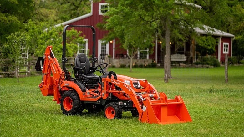 A Kubota sub compact backhoe loader parked on grass in front of a farmhouse